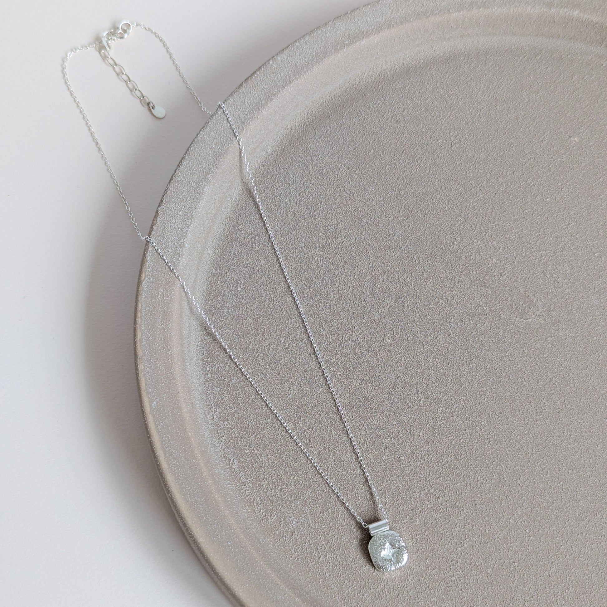 Silver star necklace with a clear pendant on a light gray plate