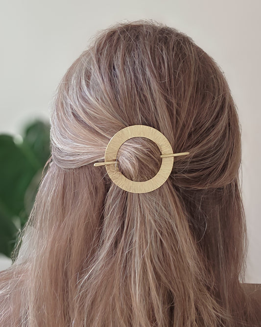 Gold circular hair clip in a person's hair with a neutral background