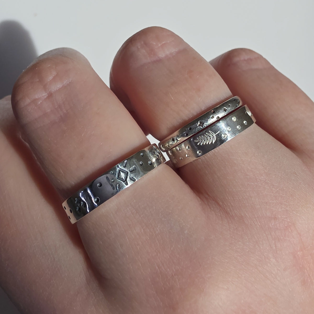 Two silver rings with textured, hammered, and engraved patterns worn on a person's fingers.