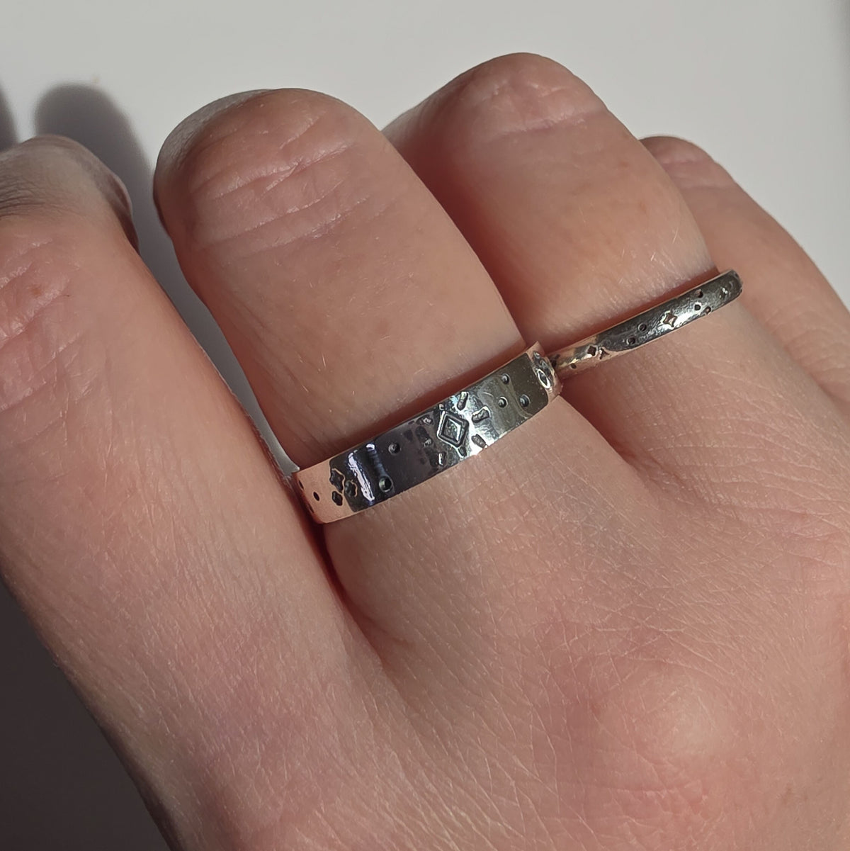 Two silver rings with textured, hammered geometric patterns worn on a person's fingers.